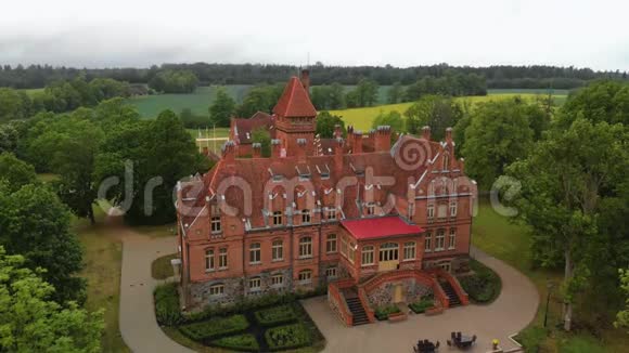 在拉脱维亚的老城堡庄园上空飞行夏季从上面俯瞰的Jaunmoku皮尔和周围的绿树视频的预览图