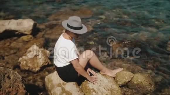 一个戴着帽子的女孩正在欣赏坐在海岸上的海洋或大海的美丽景色离那女孩不远视频的预览图