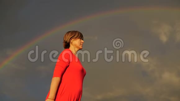 背景中的彩虹穿红色衣服的女人露出拇指和微笑视频的预览图
