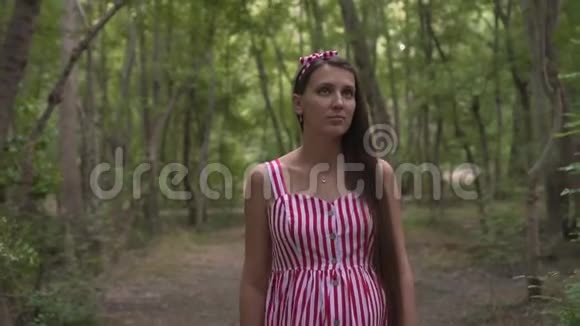 公园里绿树成荫的怀孕女孩一个穿着条纹白红色连衣裙的女孩穿过公园视频的预览图