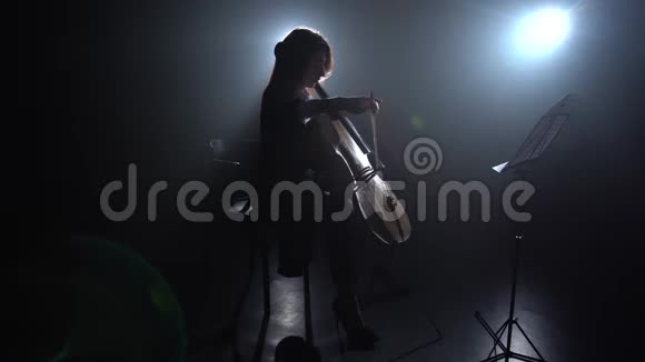 从灯光中突出一个房间女孩扮演大提琴剪影黑烟背景视频的预览图