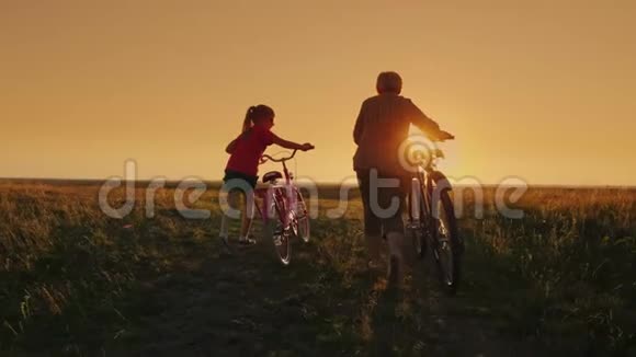 几代人的交流祖母和孙女在日落时一起去开自行车视频的预览图