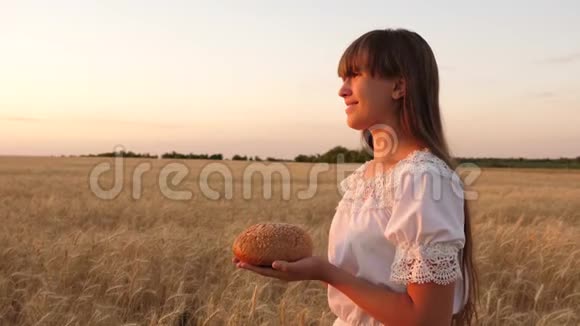 手里拿着美味的面包把一个年轻漂亮的女人抱在麦田里一个女孩手里拿着的面包视频的预览图