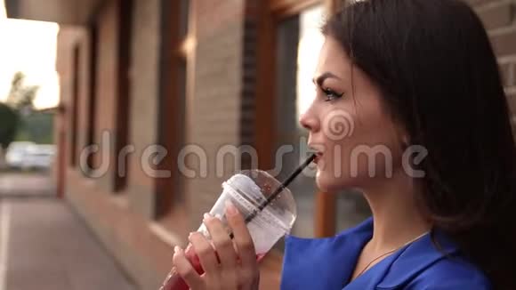 年轻迷人的女人一边喝着清爽的饮料一边走在城市的街道上视频的预览图