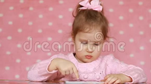 儿童外观视频和播放下载的应用程序在白色智能手机特写一个可爱有趣的小女孩看着视频的预览图