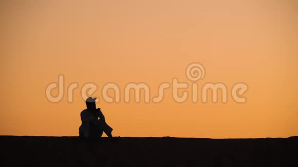 男人坐在沙丘上用手机说话视频的预览图