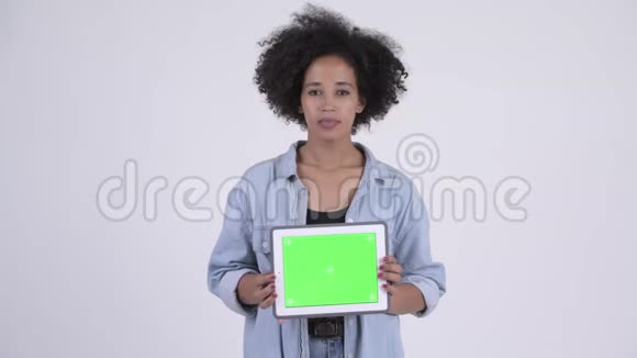 年轻快乐的非洲女人一边思考一边展示数码平板电脑视频的预览图