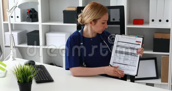 医生坐在办公椅上在文件中显示笔记看着相机视频的预览图