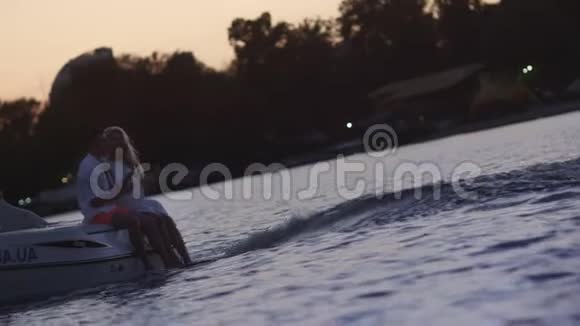 日落时分年轻人坐在漂浮的摩托艇上在游艇上的情侣视频的预览图