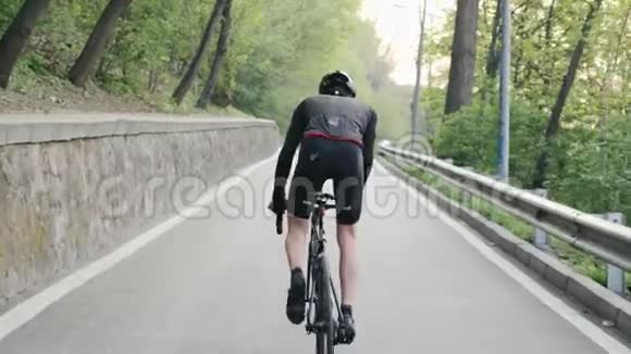 强壮的骑自行车的人穿着黑色的衣服骑着上坡的马鞍自行车训练公路自行车慢动作视频的预览图