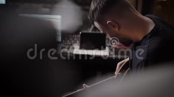 年轻的音乐家正在用吉他作曲坐在一个空的录音室里向后看视频的预览图