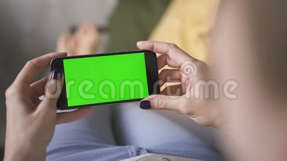 商务亚洲女人躺在家里的沙发上手里拿着一部绿色屏幕手机视频的预览图
