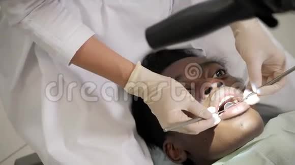 牙医通过显微镜治疗病人年轻的非裔美国男子牙科诊所的椅子视频的预览图