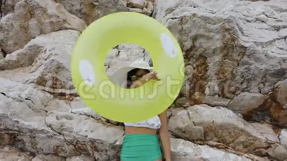 一个穿着泳衣和帽子的晒黑的女孩在她手上做了一个充气浮球圈的有趣的扭曲看着里面视频的预览图