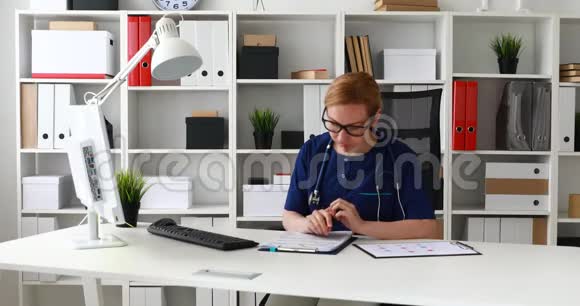 穿蓝色实验室外套的医生坐在工作场所并标记文件视频的预览图