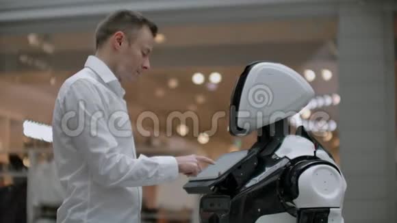 一个穿衬衫的男人和一个白色机器人交流他问问题用手指按屏幕视频的预览图