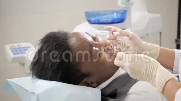 牙医在下巴上注射了一针冷冻诺瓦卡因年轻的非裔美国男子牙科诊所的椅子视频的预览图