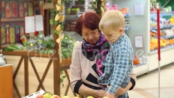一位老年妇女带着她的小孙子在大型超市买新鲜苹果视频的预览图