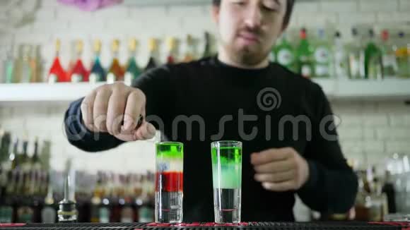 酒吧老板手里拿着打火机在酒吧桌上放着一杯彩色的酒精饮料视频的预览图