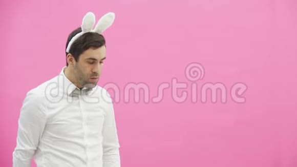 年轻英俊的男孩站在粉红色的背景上一个头上长耳朵的人一个男人拿着胡萝卜把它放进去视频的预览图