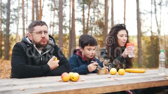 妈妈爸爸和孩子在餐桌旁的树林里坐在一起享受美食视频的预览图