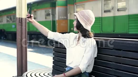 快乐亚洲女乘客与休闲自拍智能手机在火车站轨道旅行视频的预览图