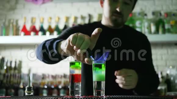 酒吧表演手里拿着打火机的男人在酒吧桌上用薄薄的玻璃装饰着彩色的酒精饮料视频的预览图
