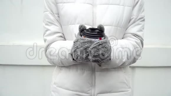 女人用灰色羊毛手套暖手冬天喝杯咖啡或茶白色背景带走视频的预览图