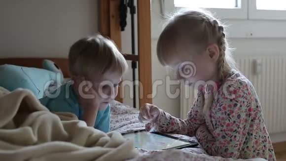 小孩子在床上玩平板电脑游戏微笑视频的预览图