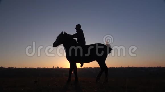 骑手坐在马上在日落时给他两条腿慢动作剪影侧视图视频的预览图