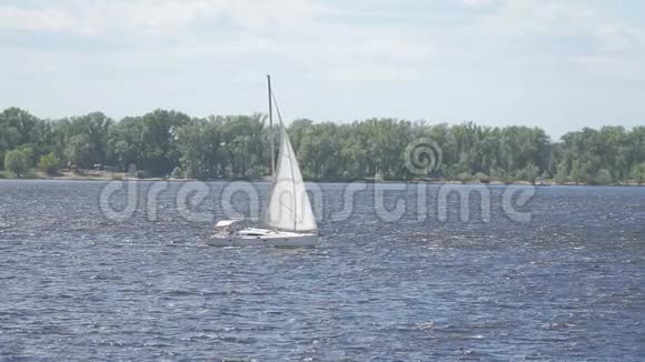 一艘白色的帆船在岸边一片森林的背景下沿着河流航行视频的预览图