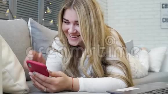 穿着睡衣的漂亮年轻女人手里拿着智能手机一边在屏幕上打字一边在活人面前聊天视频的预览图