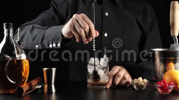 老式鸡尾酒酒保用酒保勺子把糖安格斯图拉和冰块混合在岩石玻璃中玻璃冷却了视频的预览图