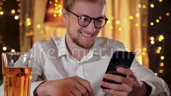 一个长胡子的帅哥在酒吧喝啤酒的时候用智能手机微笑着视频的预览图
