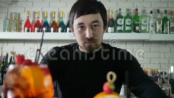 一幅美丽的男性肖像旁边是生动的酒精饮料浆果在酒吧内部的柜台上瓶子是白色的视频的预览图