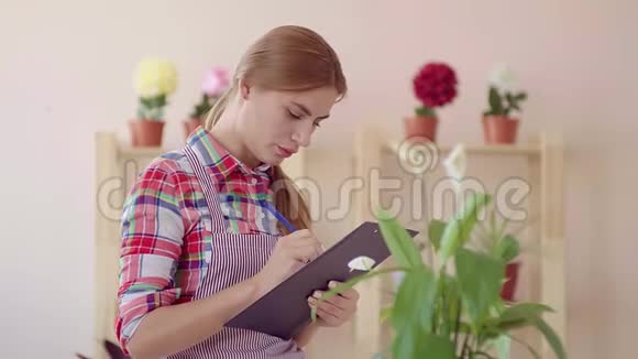 小生意开一家花店一个穿着格子衬衫和条纹围裙的女孩拿着文件夹写着视频的预览图