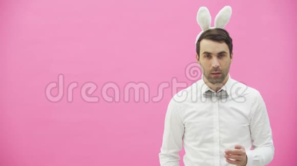 年轻英俊的男孩站在粉红色的背景上一个头上长耳朵的人一个男人拿着胡萝卜把它放进去视频的预览图