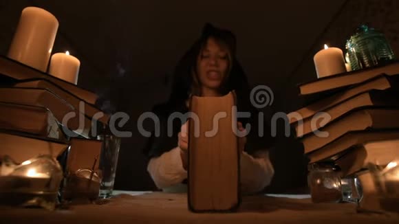 一位无聊的女魔术师在烛光下的一间黑暗的房间里特写涉猎一本书沉思低键带电摄像机视频的预览图
