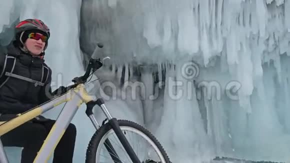 人们坐在冰窟附近的自行车旁有冰洞和冰柱的岩石非常美丽骑自行车的是视频的预览图