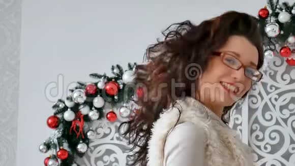 圣诞装饰背景下一个穿着眼镜和温暖毛衣的快乐黑发女孩的肖像可爱的女孩视频的预览图