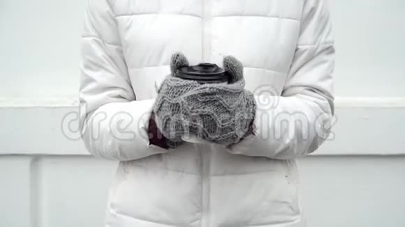 女人用灰色羊毛手套暖手冬天喝杯咖啡或茶白色背景带走视频的预览图
