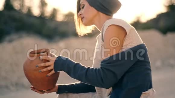 年轻迷人的穿着民族服装的女人坐在路边从水罐里倒出沙子水变成了沙子视频的预览图