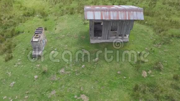 4k无人驾驶飞机在森林边绿色高地上的小木屋上空摄像机顺着地面向下攀爬视频的预览图