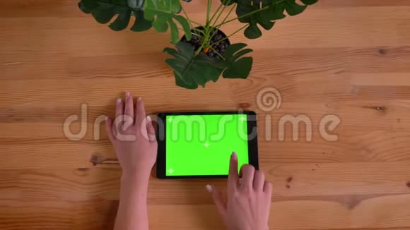 顶部拍摄的女性手触摸绿色屏幕的水平平板在木桌和植物背景视频的预览图