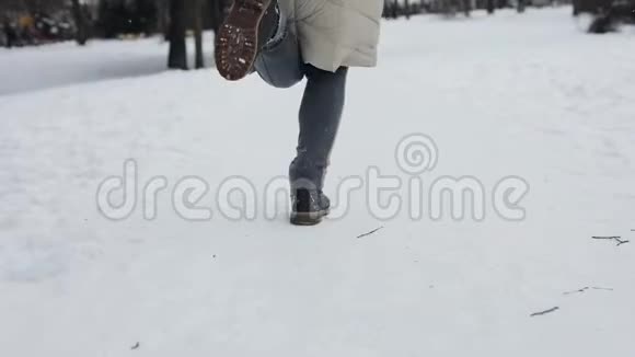 穿着米色羽绒服和时髦靴子的女人在下雪的中央公园里奔跑下雪了慢动作后景视频的预览图