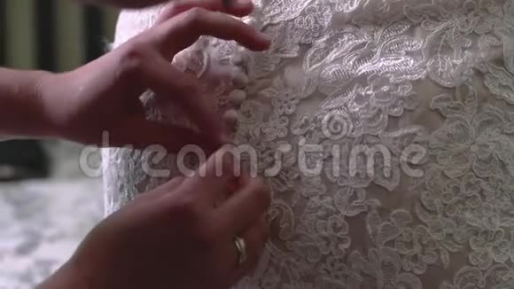 伴娘帮助新娘关闭花边婚纱上的纽扣视频的预览图