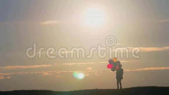 日落时分坐着气球在田野里散步的剪影女孩日落时带着气球在田野里快乐的孩子视频的预览图