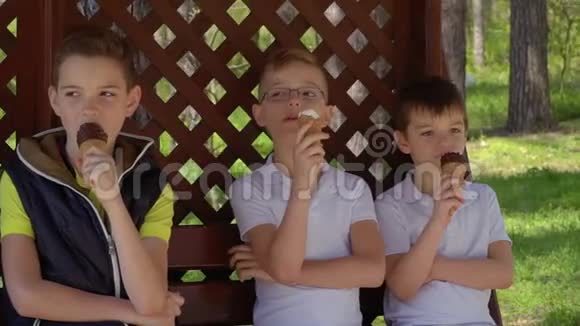 三个可爱的男孩在长凳上的凉亭里吃冰淇淋视频的预览图