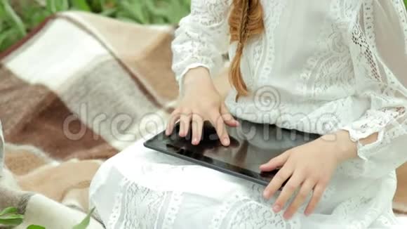 穿着老式衣服的女孩坐在野餐上拿着一篮子苹果慢悠悠地看着平板电脑视频的预览图