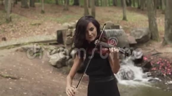 穿着漂亮的女孩在森林里拉小提琴背景是瀑布视频的预览图
